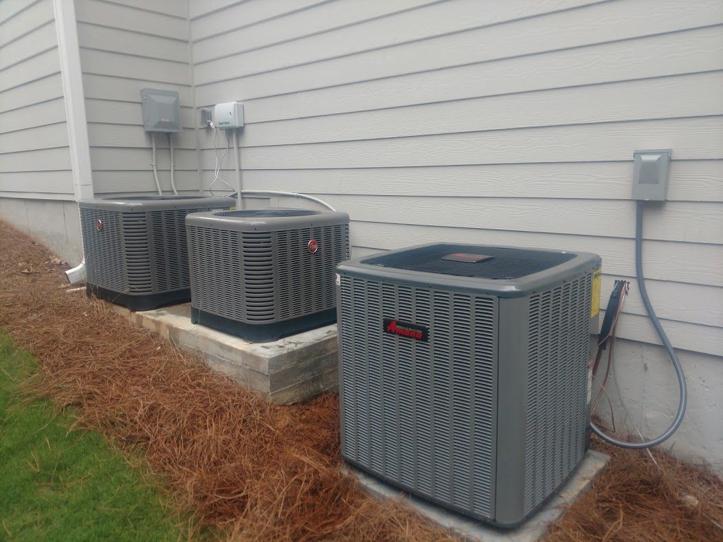 A technician in a white shirt and camouflage hat installs wiring on a Carrier brand air conditioning unit on a flat roof.