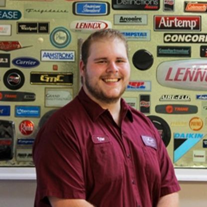 A person wearing a maroon collared shirt smiles in front of a wall covered in various HVAC equipment brand logos.