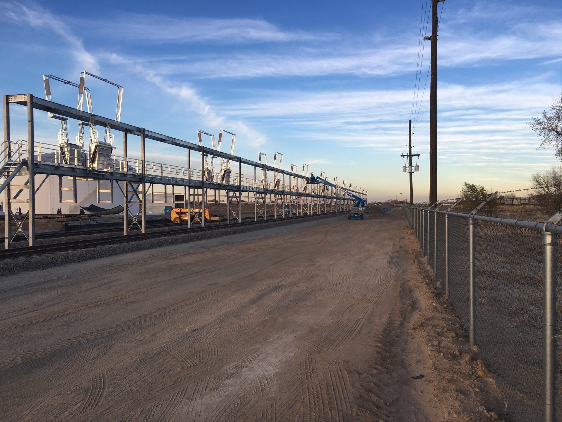 a dirt road with a chain link fence leading to a train yard