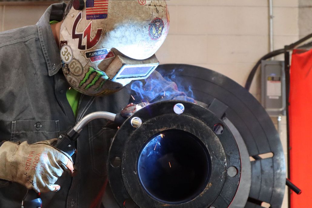 a man wearing a welding mask is welding a pipe .