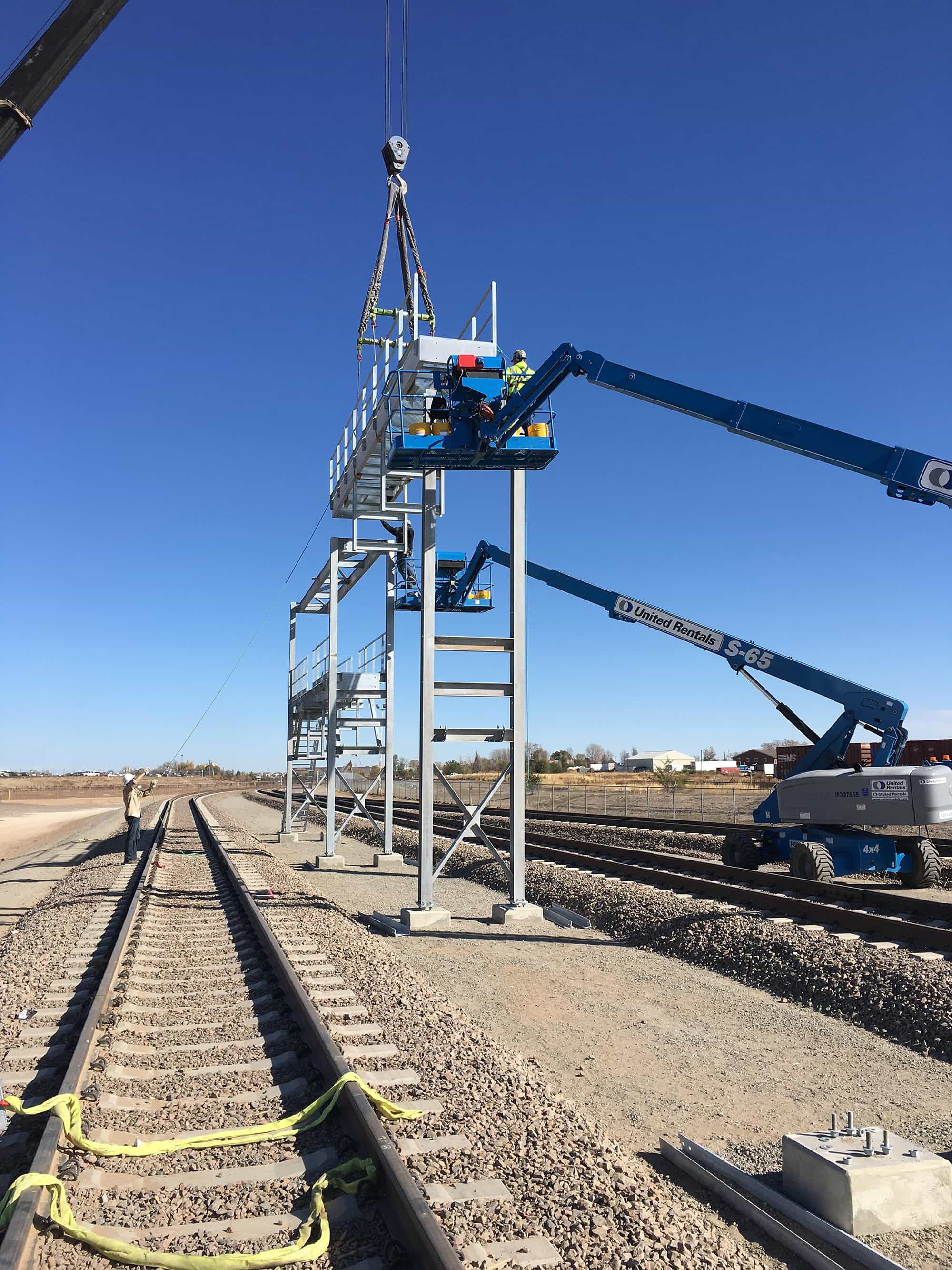 a group of people are working on a bridge over train tracks.