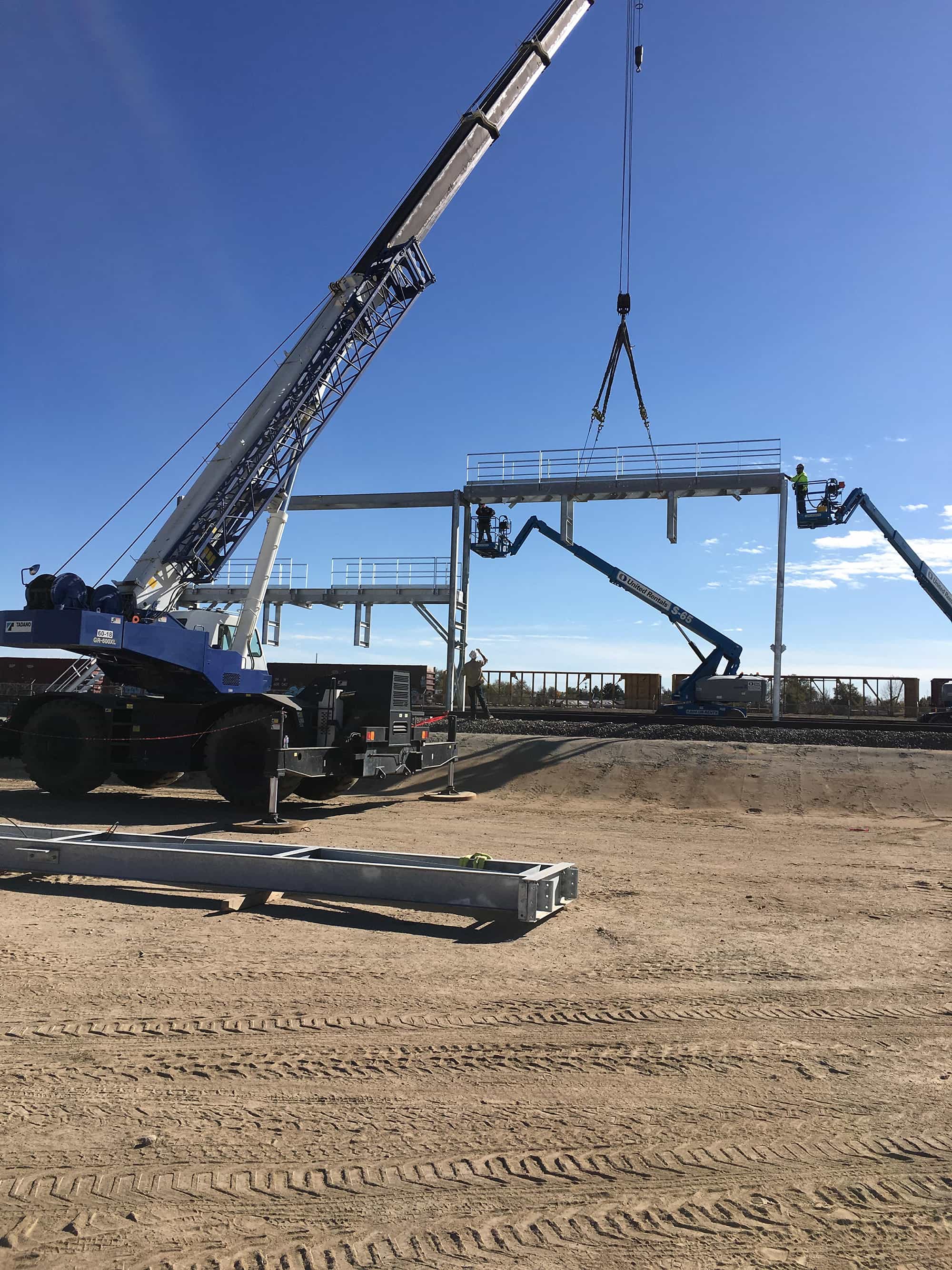 a crane is lifting a metal structure in a dirt field .