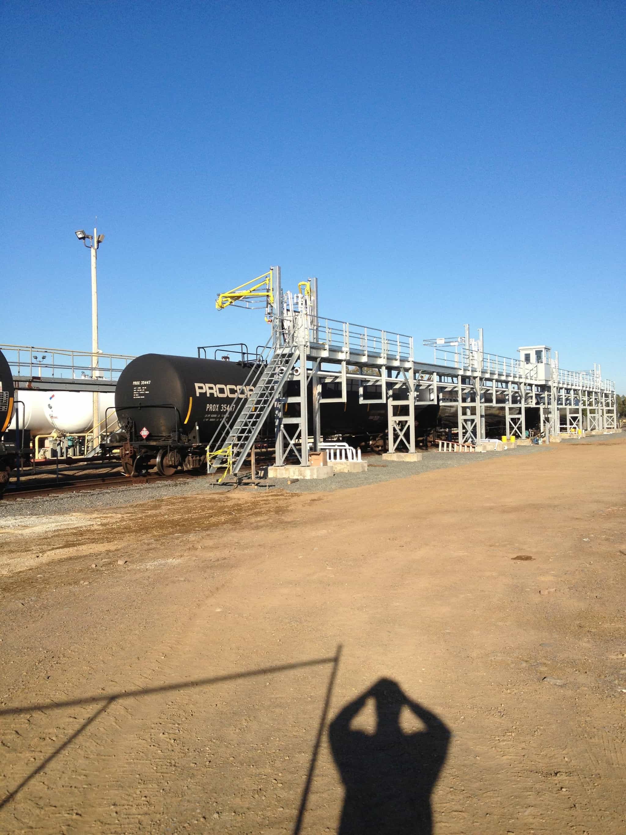 a shadow of a person is cast on the ground in front of a train yard