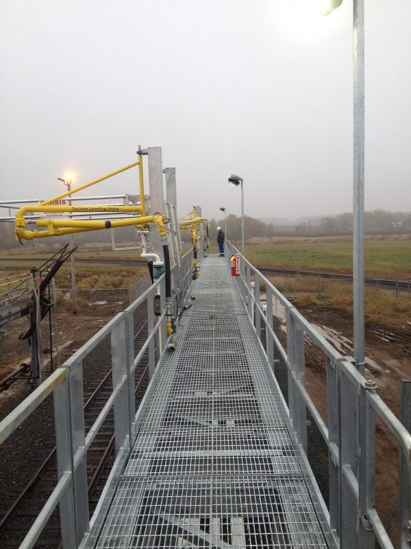 a metal walkway leading to a train track on a foggy day.