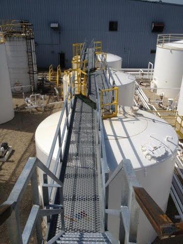 a metal walkway leading to a row of tanks in a factory.