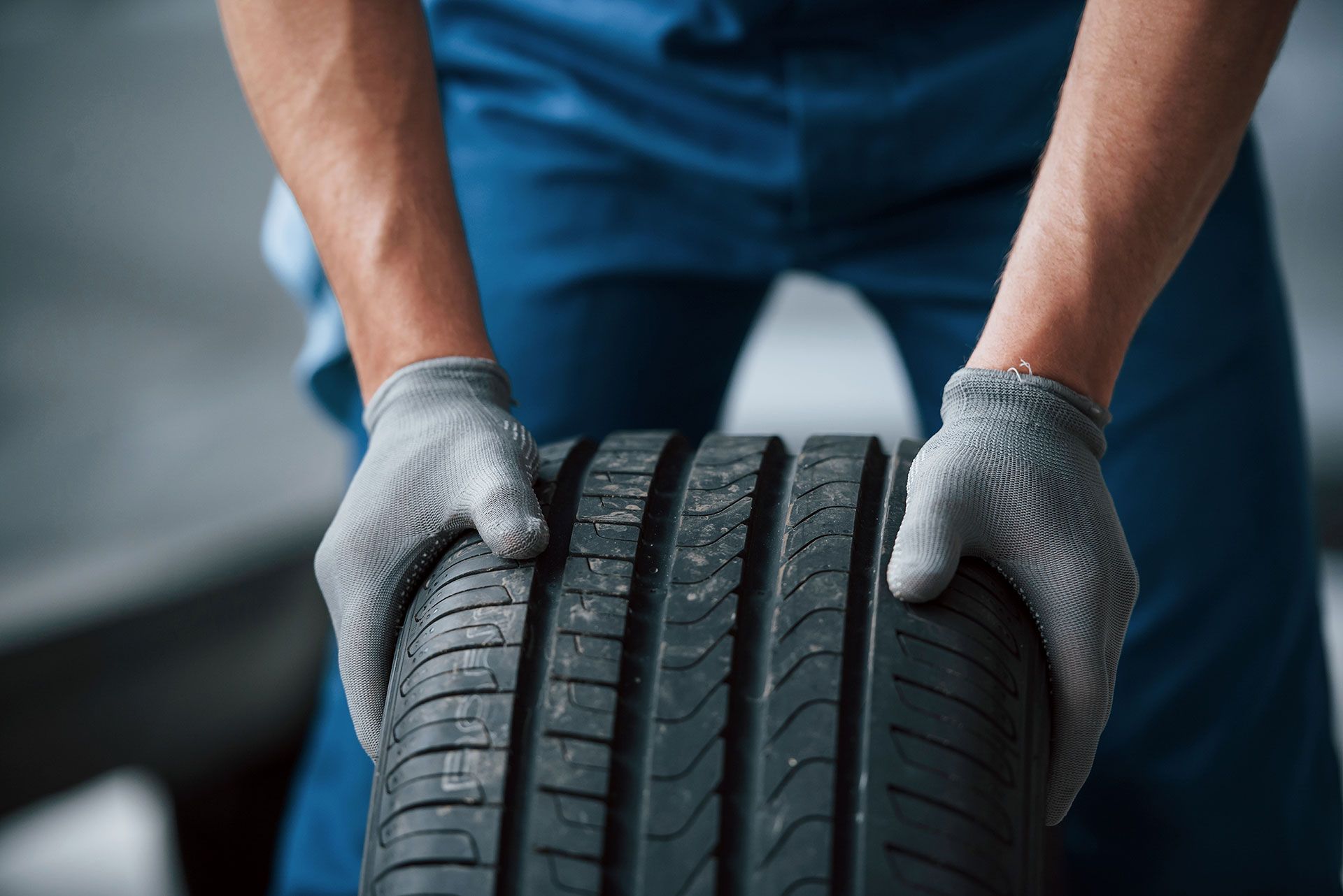 A man wearing gloves is holding a tire in his hands.