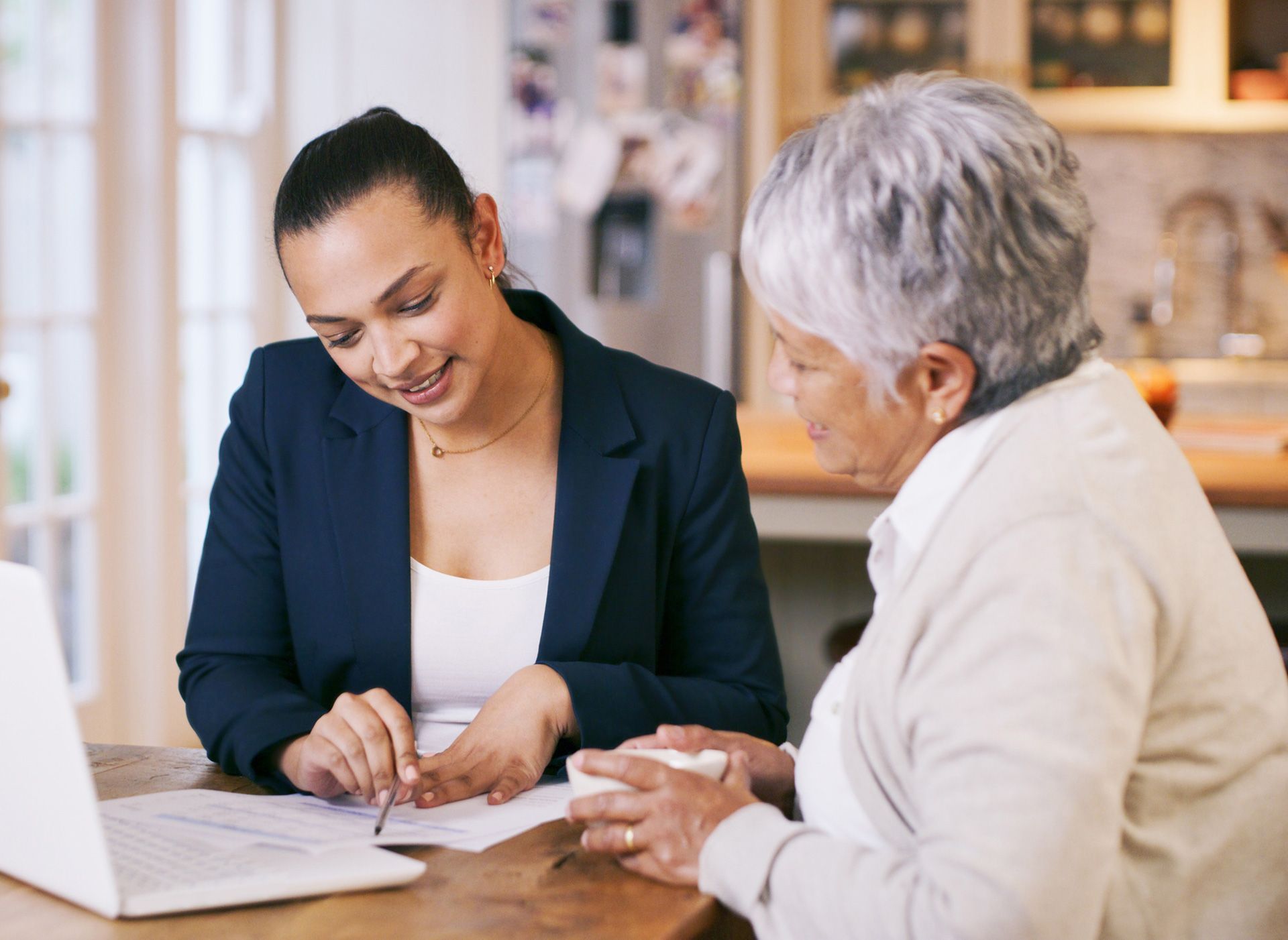 Two women are sitting at a table looking at a laptop.