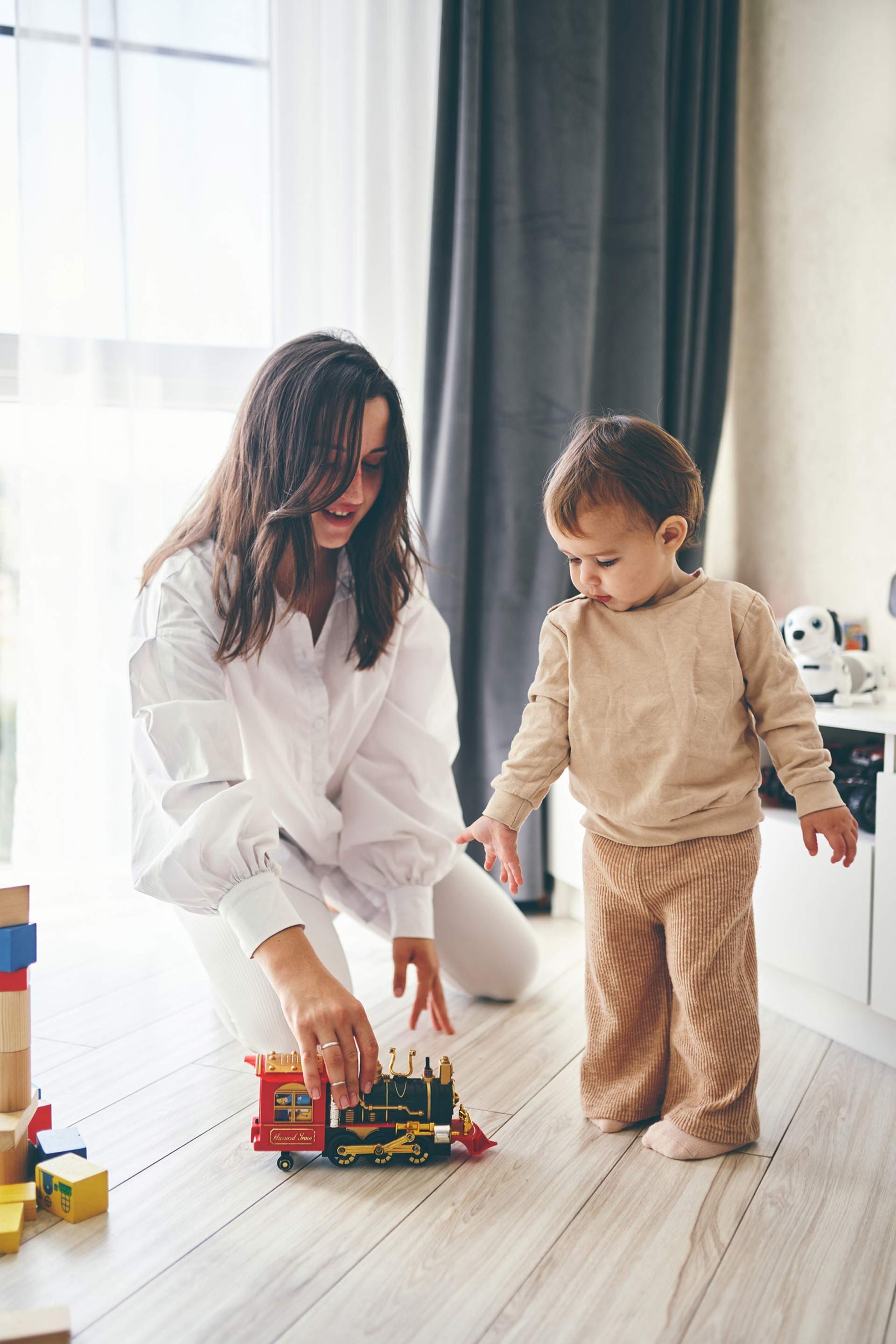 A woman and a child are playing with a toy train on the floor.