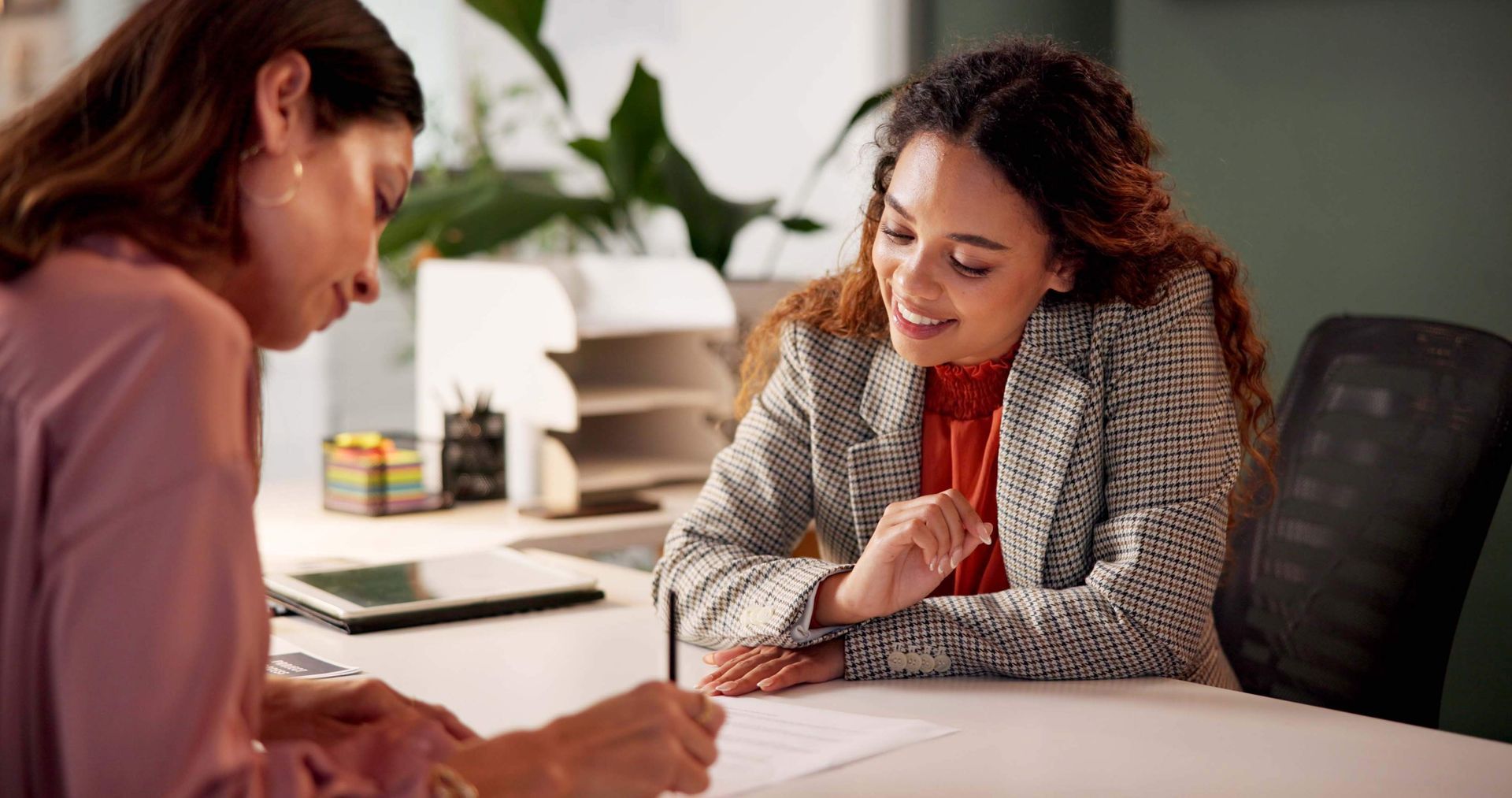 Two women are sitting at a table signing a document.