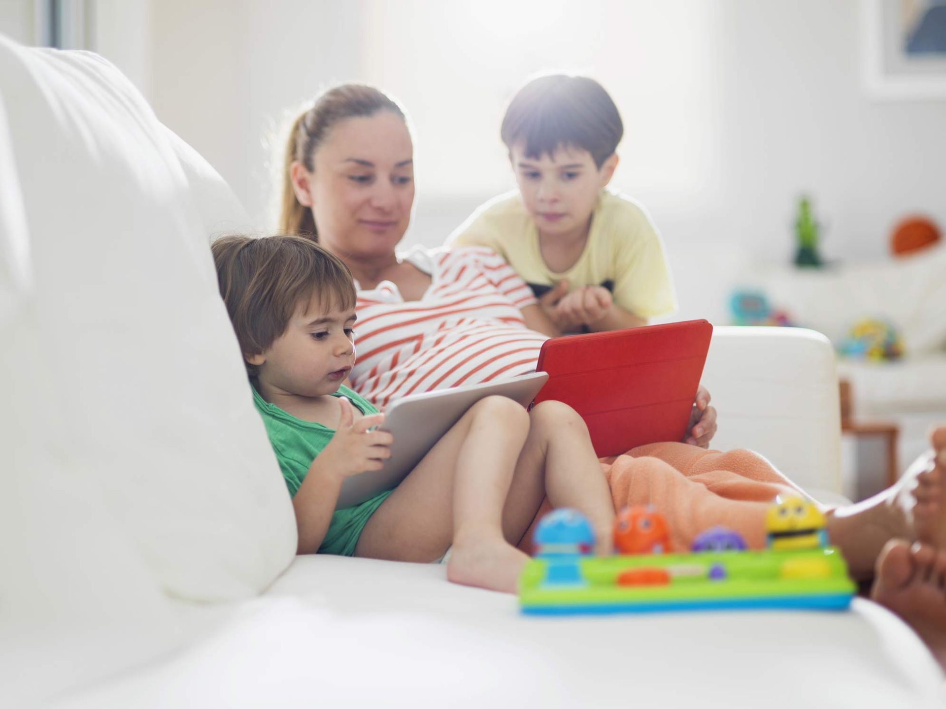 A woman is sitting on a couch with two children and a tablet.