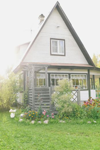 A small white house with a black roof and a porch in a garden.