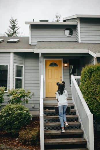 A woman is walking up the stairs of a house with a yellow door.