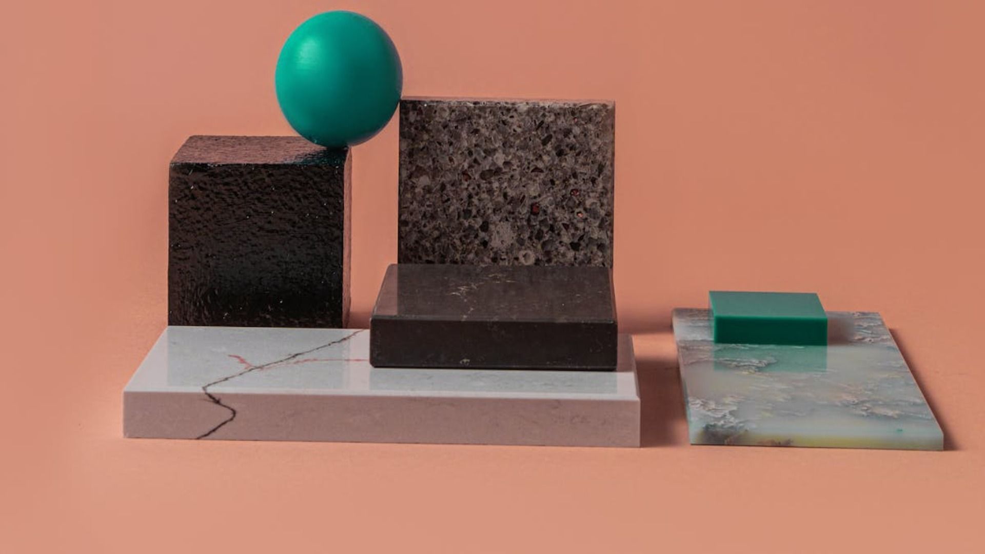 Disposición de bloques texturizados y esfera verde azulado, con fondo coral.