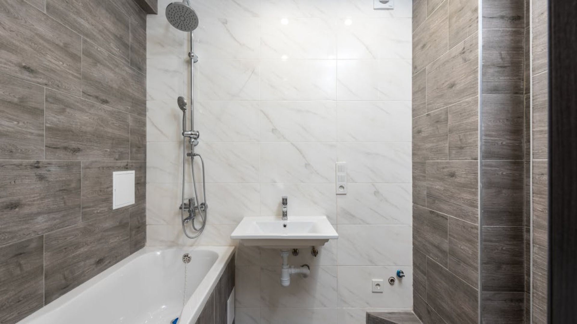 Baño con bañera, lavabo y ducha. Paredes de azulejos grises y blancos.