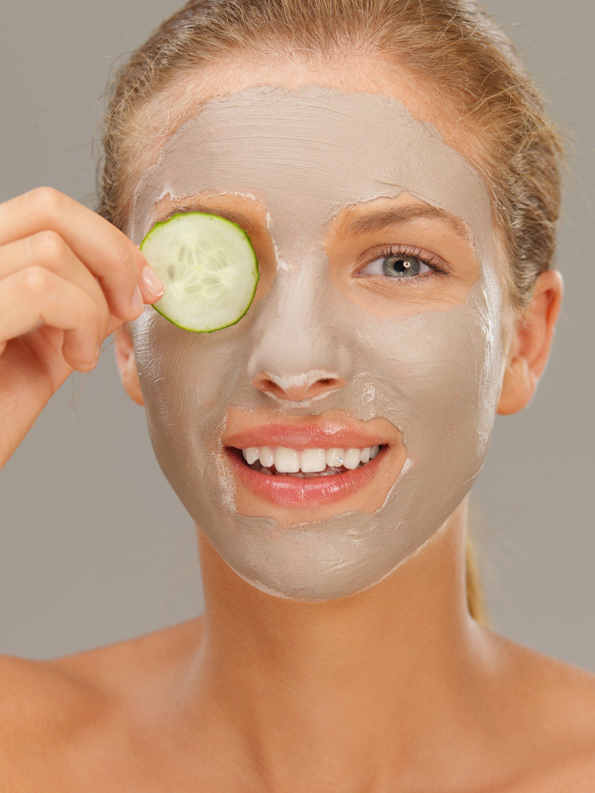 A woman holding a cucumber on her eyes as she wears a facial mask