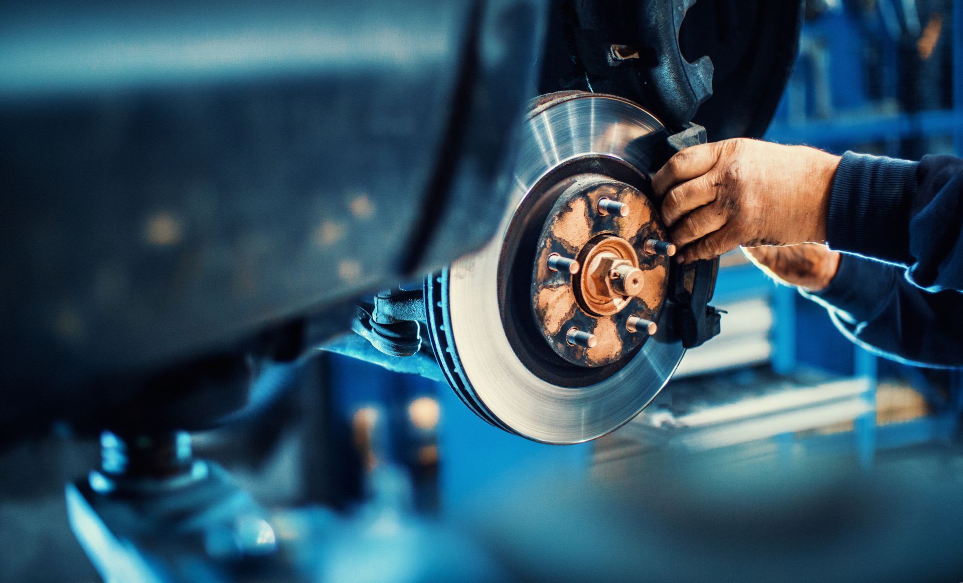 Mechanic replacing car brake pads in auto repair shop, car lifted with hydraulic jack, closeup view