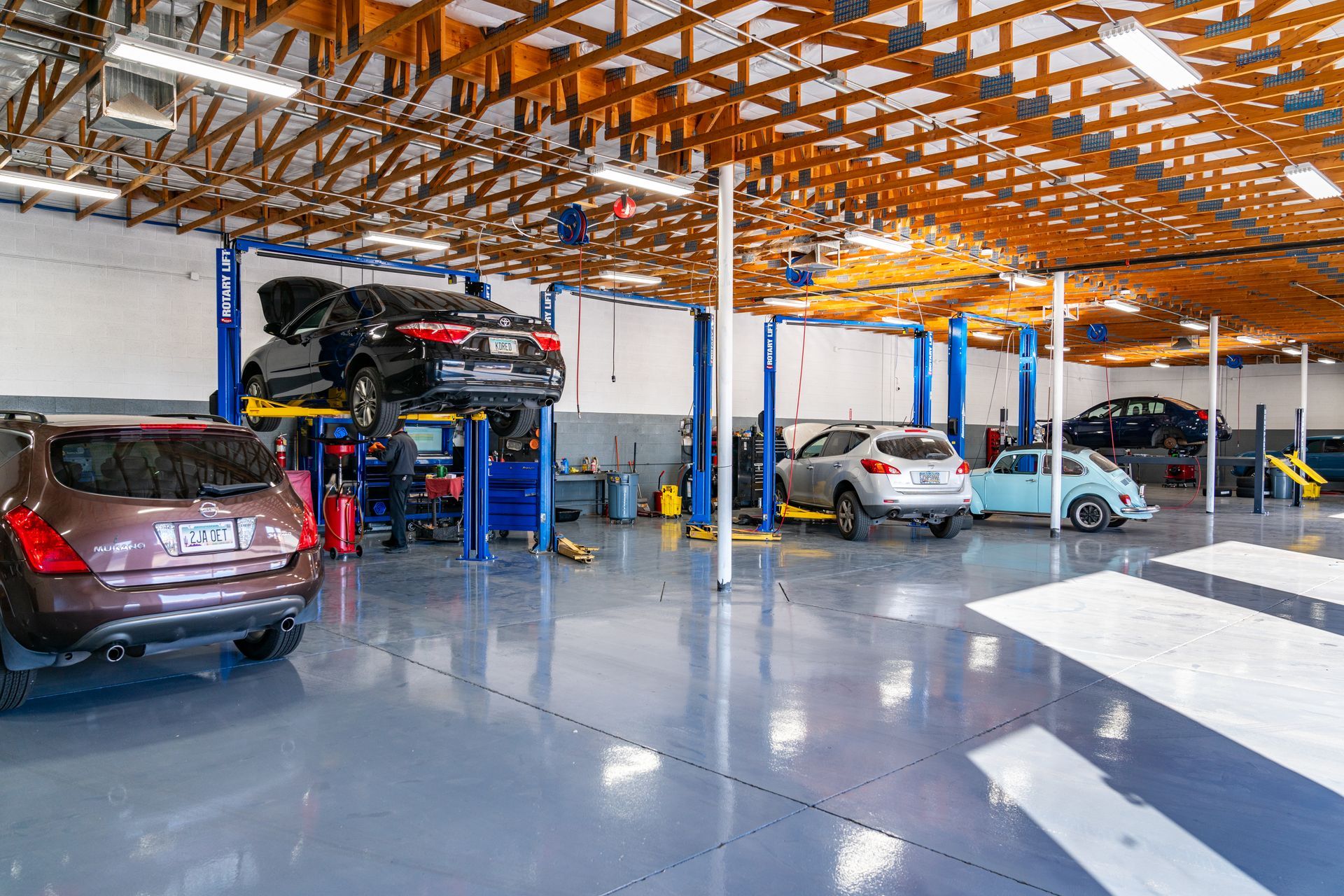 Inside a bright auto repair shop; cars on lifts, mechanics working, blue and gray colors.
