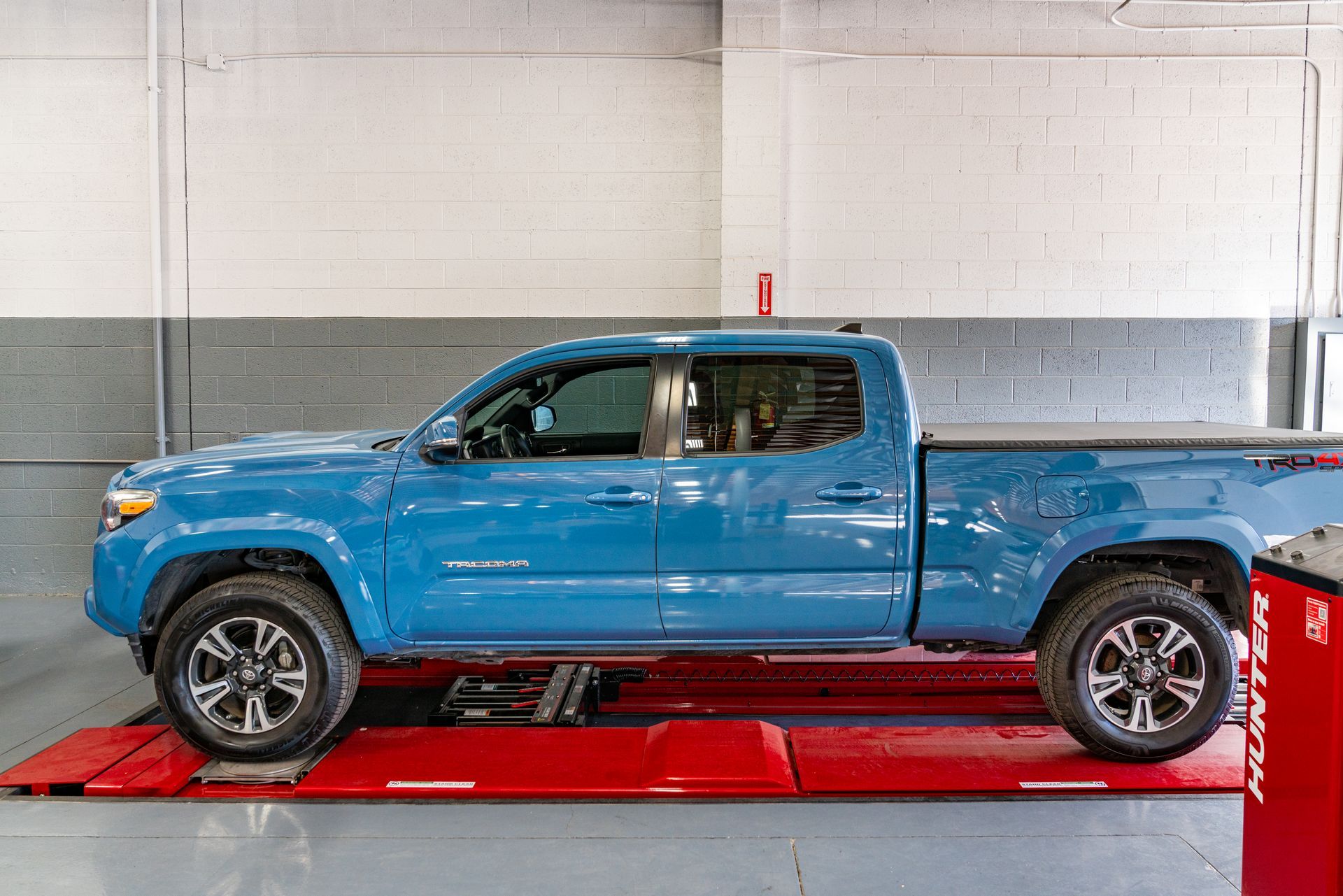 Blue Toyota Tacoma pickup truck in a shop on a red lift.