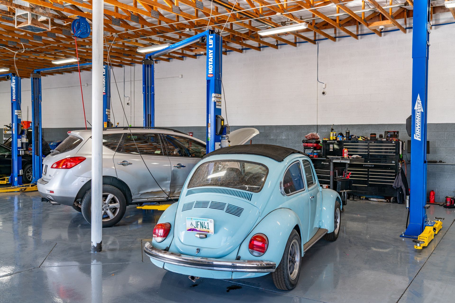 A light blue vintage Volkswagen Beetle and a silver SUV inside an auto repair shop with lifts.