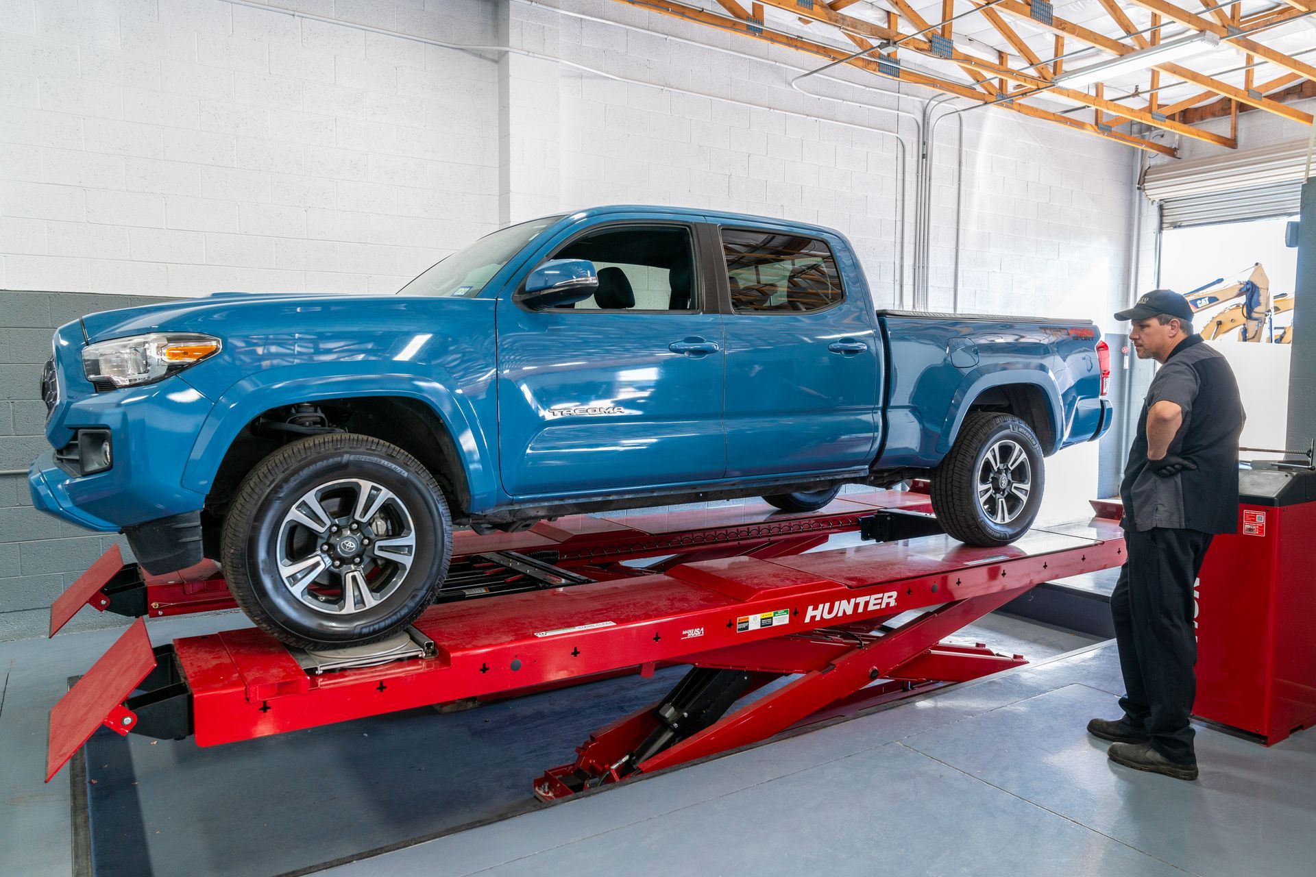 Blue pickup truck on a red lift in a garage, a mechanic looks on.