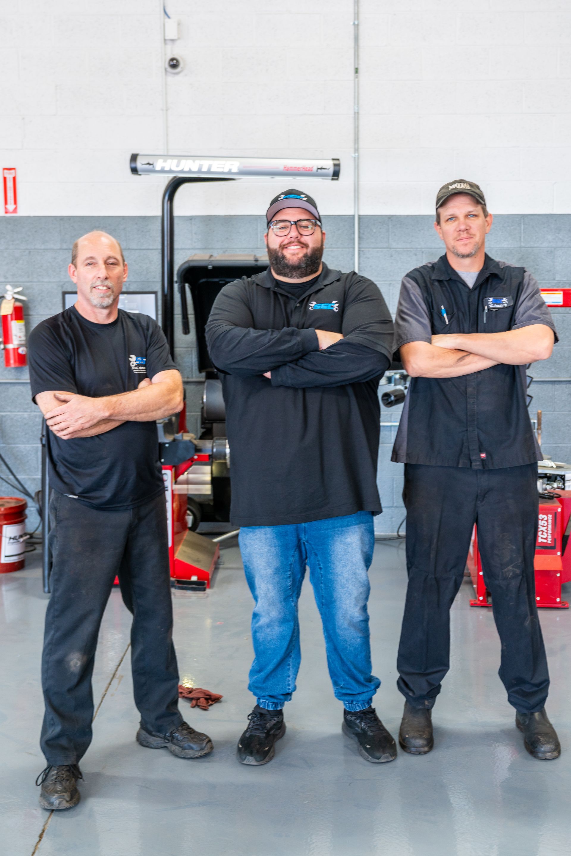 Three auto mechanics in a garage, arms crossed.