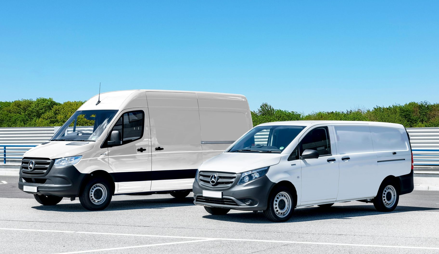 Two white Mercedes-Benz vans parked on asphalt under a blue sky. One larger, one smaller.