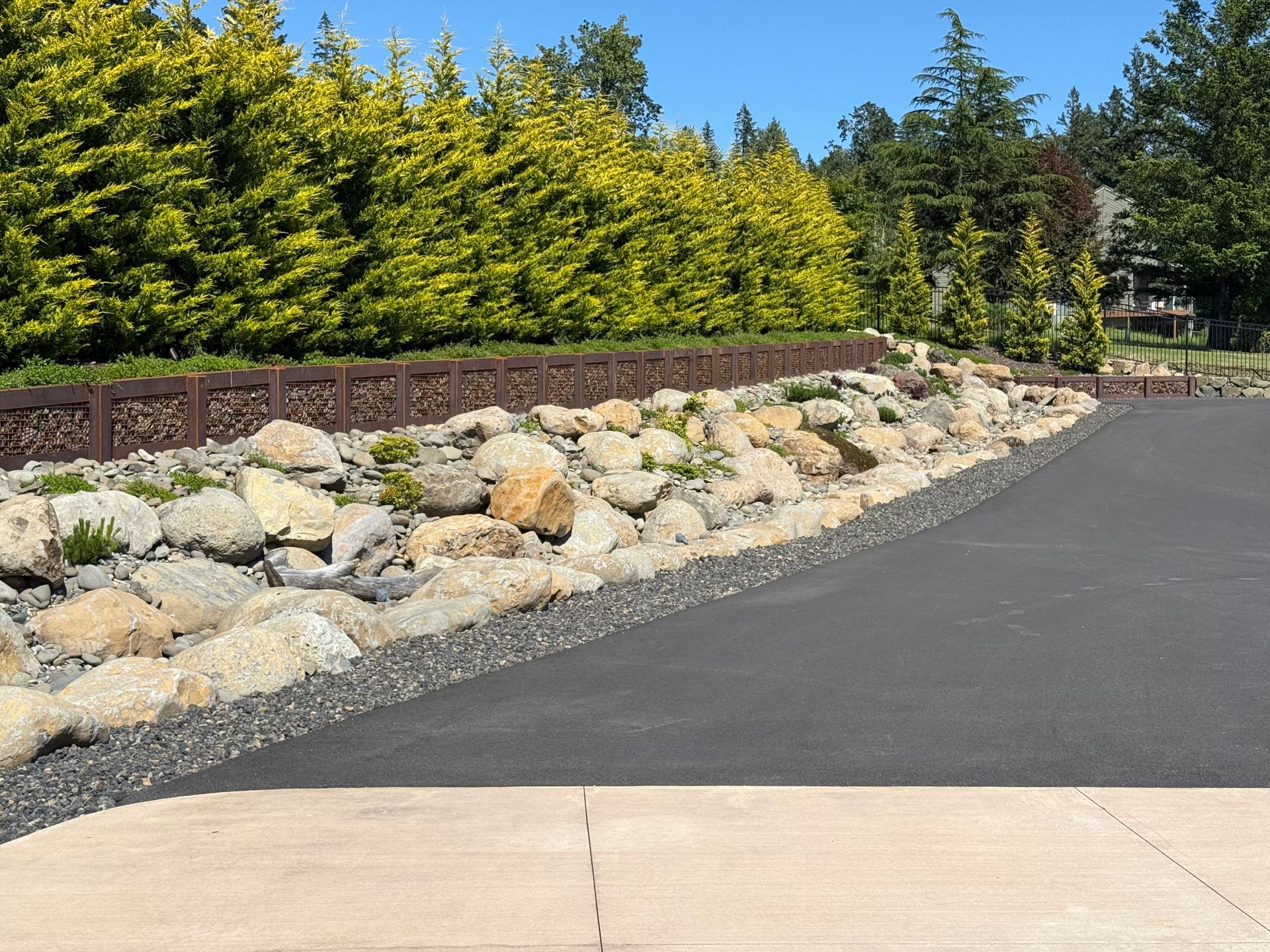 Custom home driveway with boulder landscaping, black gravel, and privacy trees.