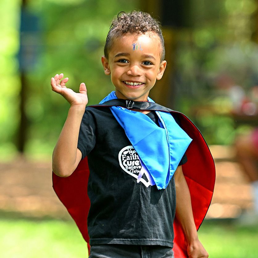 A little boy weraing superhero gear waves and smiles at last year's walk