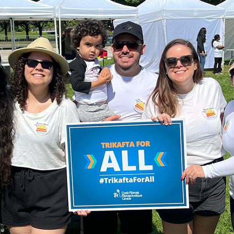 Helio and his son Oscar, who has CF, at the 2025 Walk, holding a sign that says, Trikafta For All.
