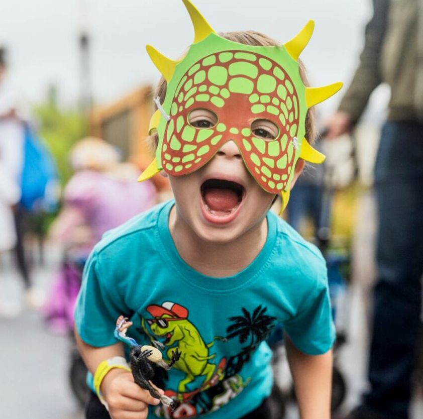 A little boy wearing a dinosaur superhero mask