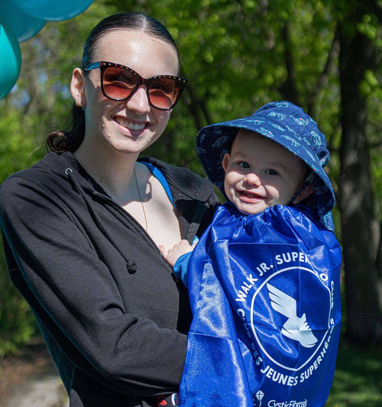 A mom holding her toddler who's wearing the Walk Jr. Superhero cape.