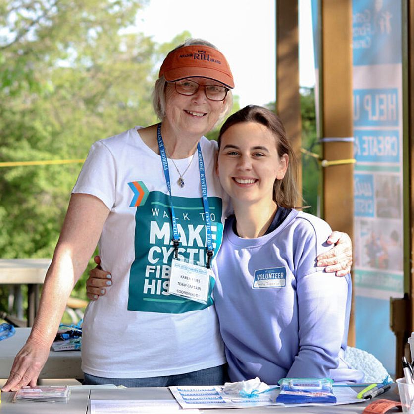 An older woman and a young woman who are volunteering for the Walk join arms and smile