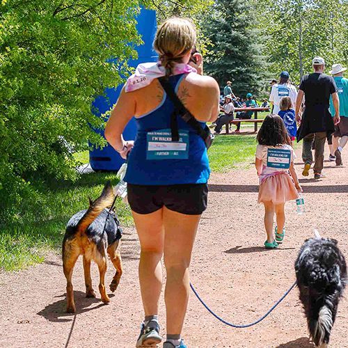 A walker and her dog walk along a dirt path in a picnic area at The Walk.
