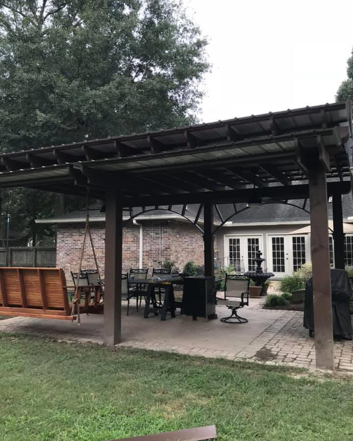 Patio with pergola, swing, dining table, and chairs. Brick house in background, overcast day.