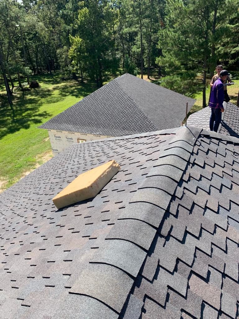 View of a roof with dark gray shingles and a person in purple on the roof.