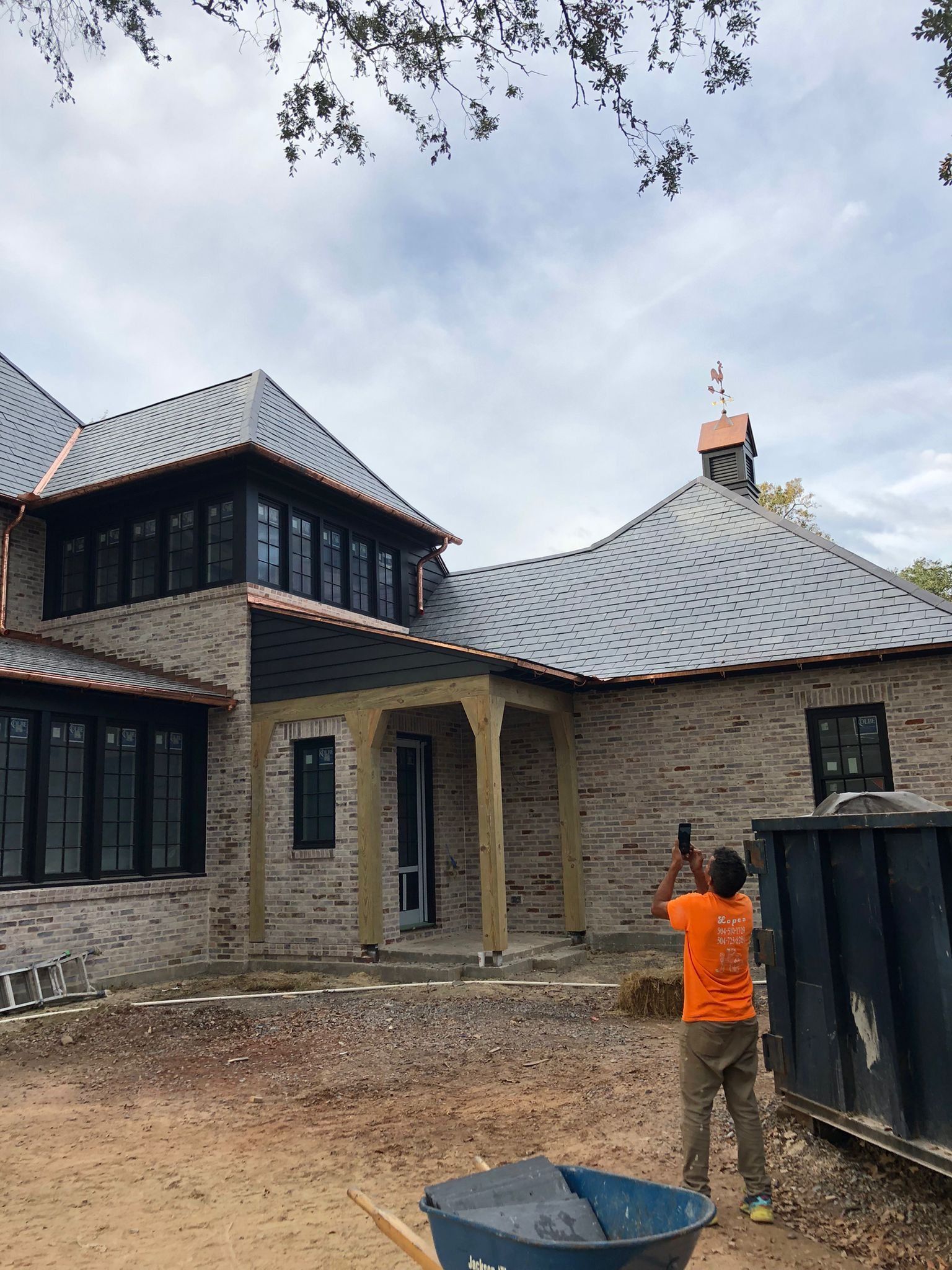 Person taking photo of brick house with tiled roof; construction site.