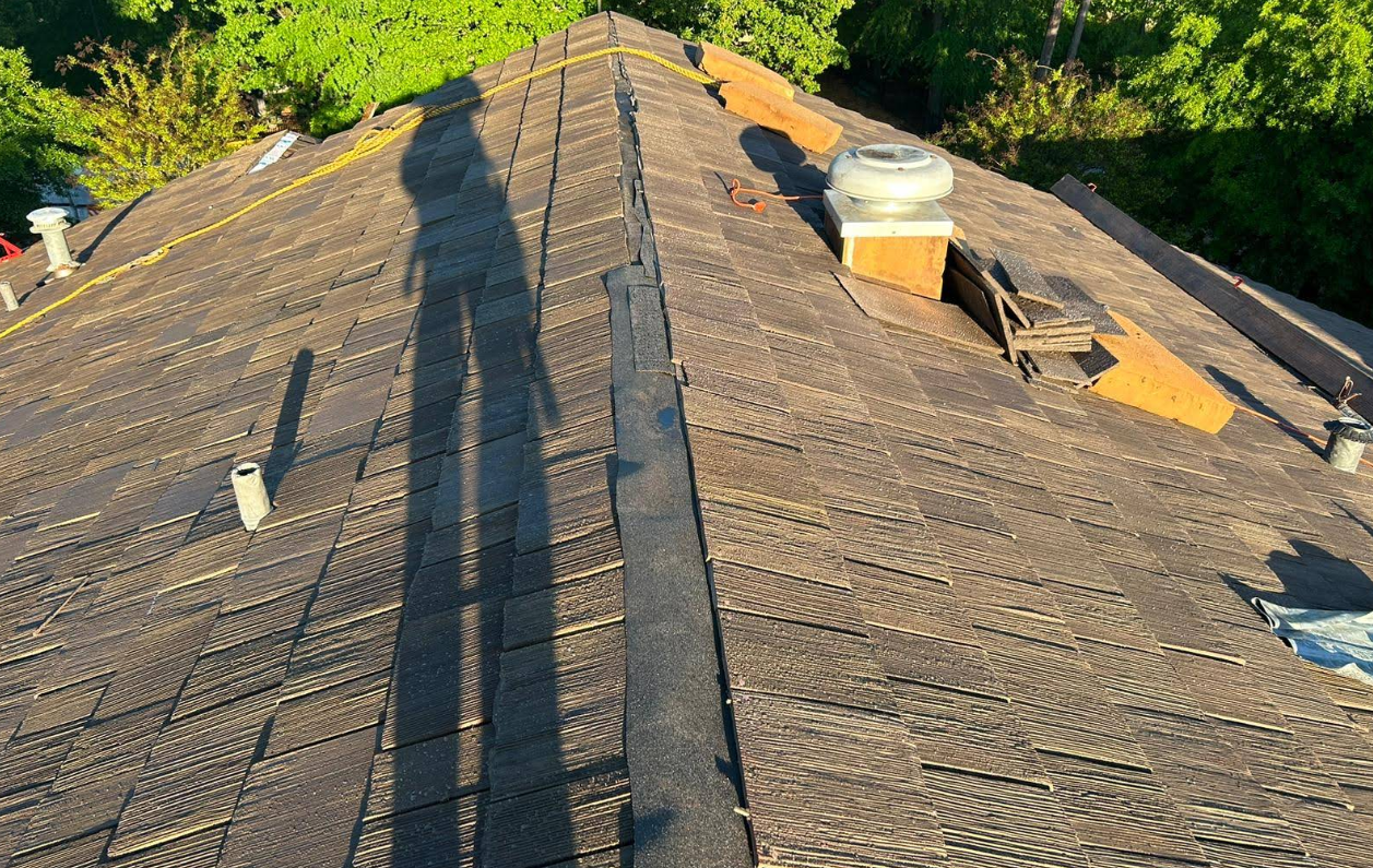 Rooftop view with brown shingles, chimney, and a long shadow of a person.