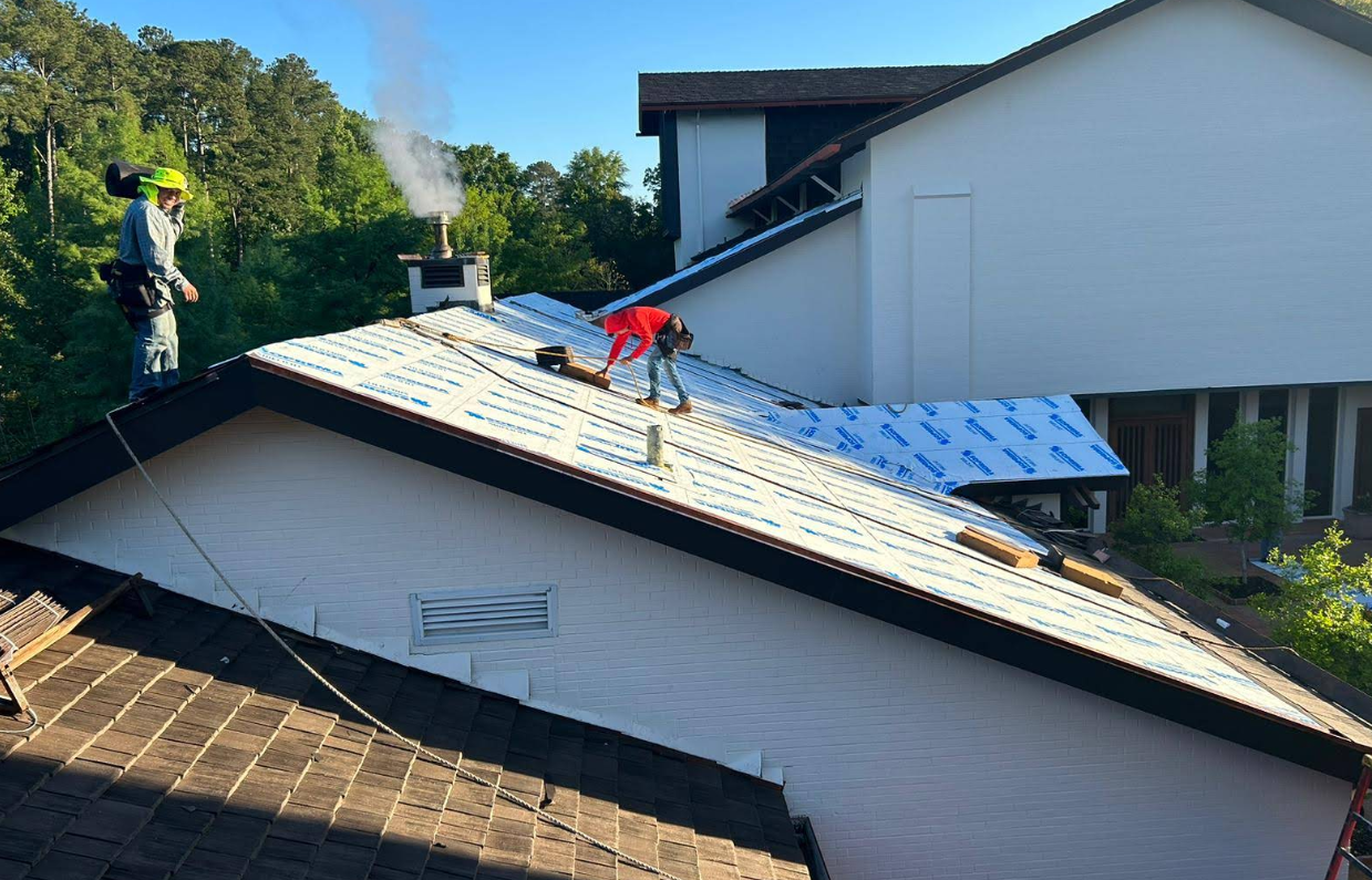 Roofers working on a residential roof, some with smoke rising from a chimney, sunny outdoors.