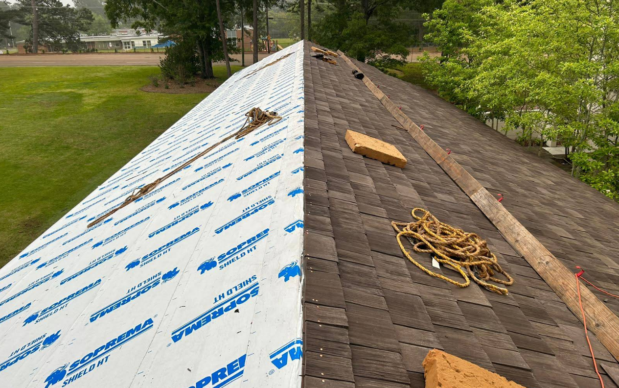 A roof partially covered with new white underlayment and old, weathered shingles, construction in progress.