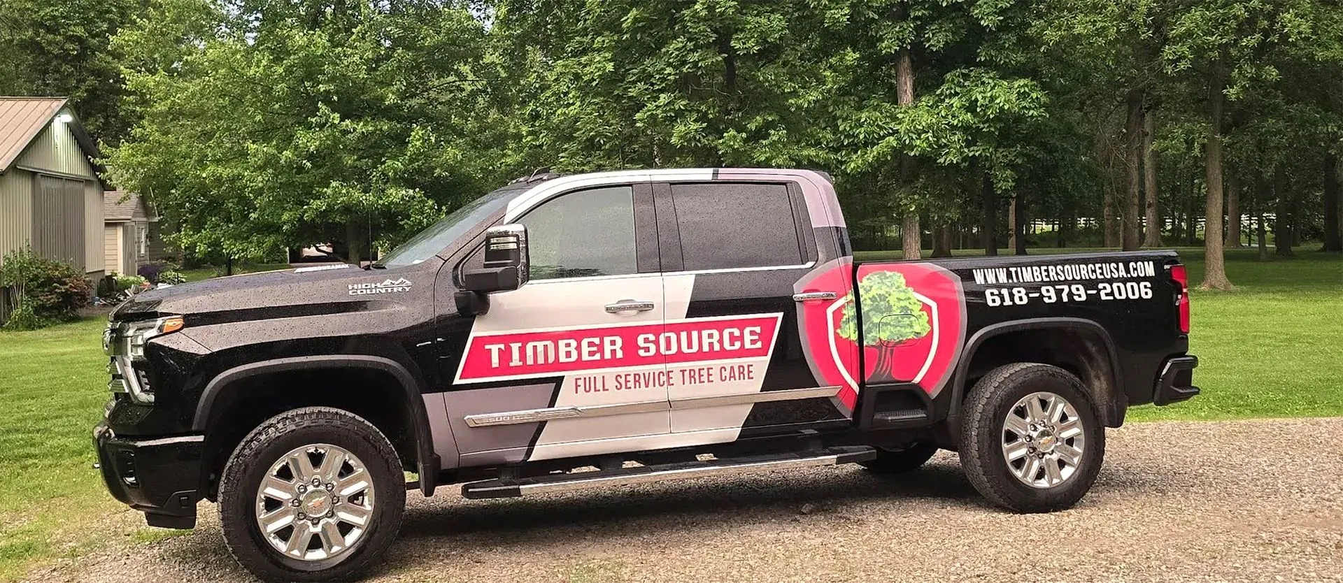 Black pickup truck with Timber Bounce logo parked on gravel. Green trees and shed in background.