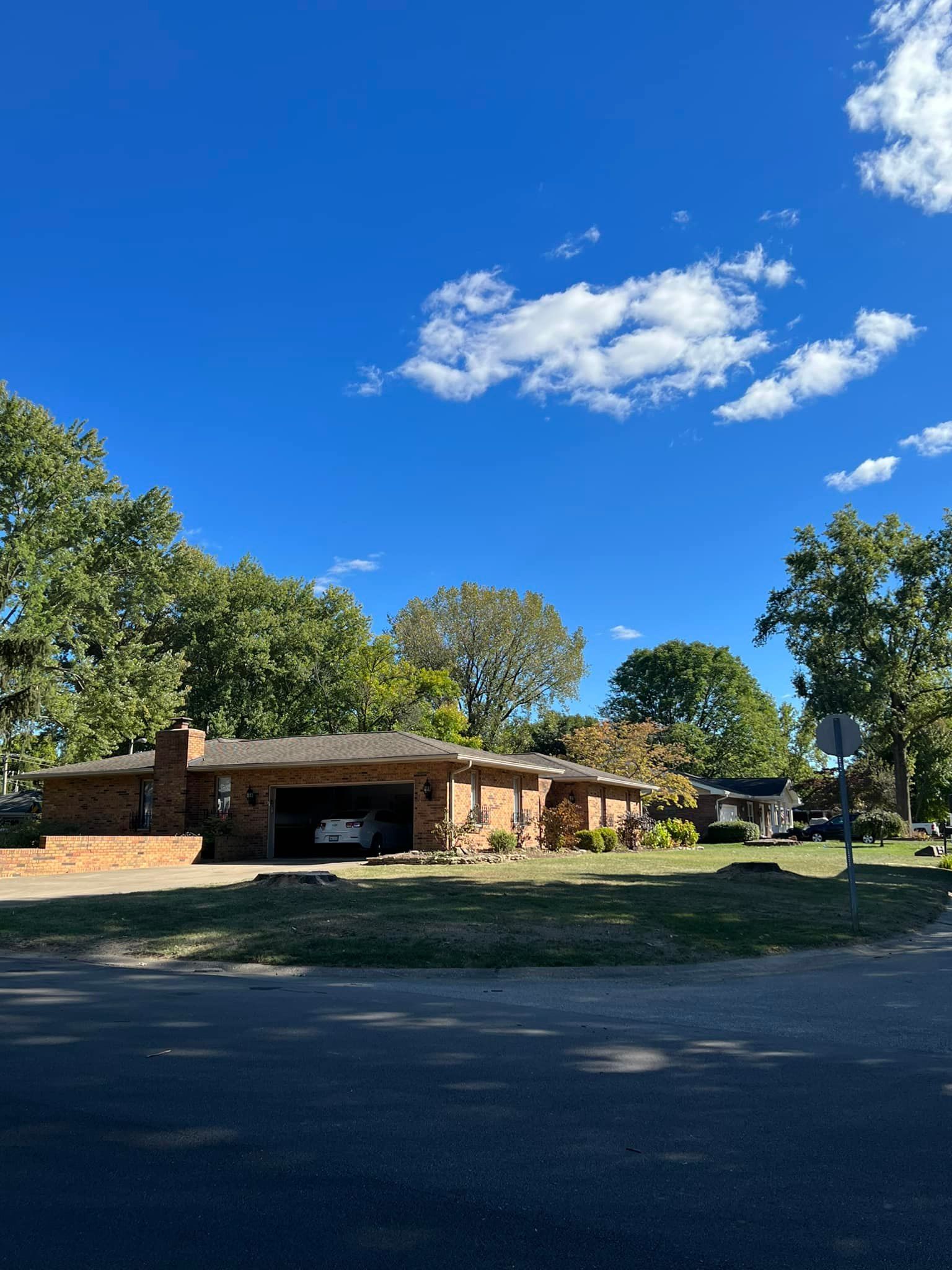 Brick house with attached carport, sunny day, blue sky, trees in background.