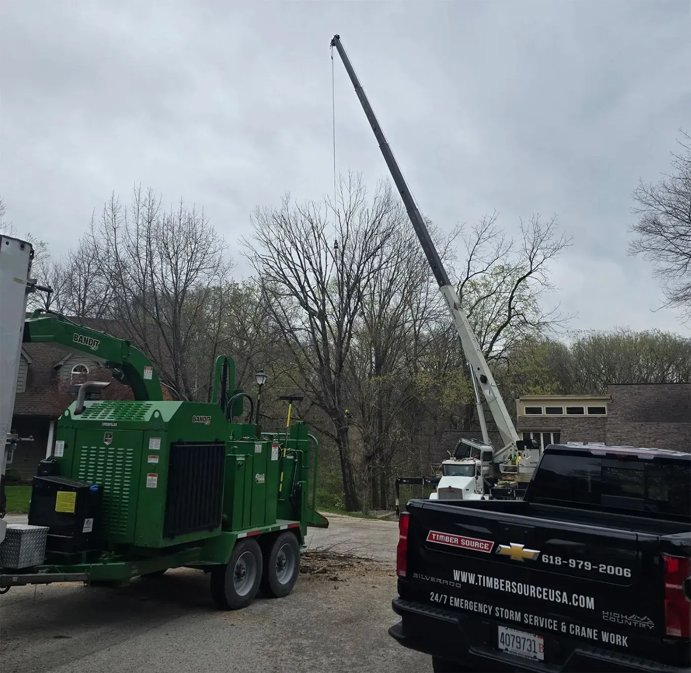 A crane lifts debris as a wood chipper and truck are present. Exterior shot. Overcast day.
