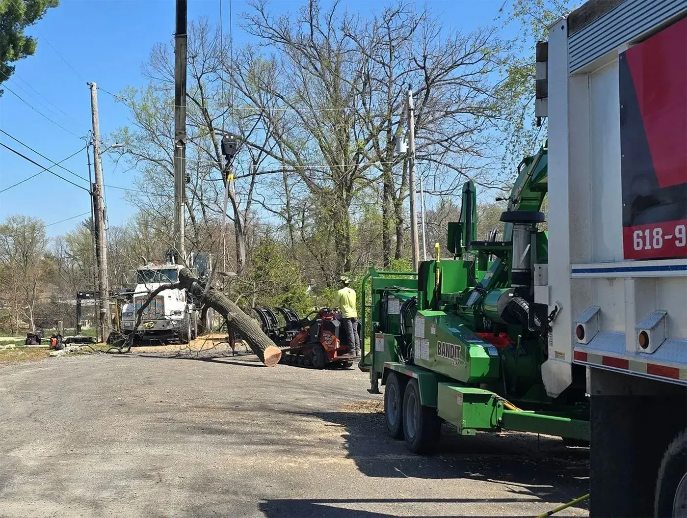 Tree service clearing debris. Green chipper, truck, and workers near power lines.