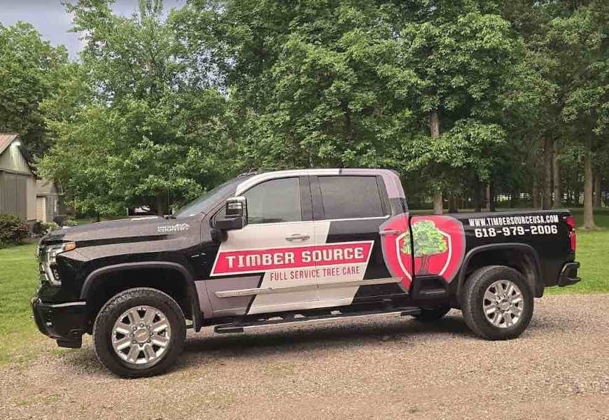 Black truck with Timber Source logo parked outdoors. Company information on side and back.