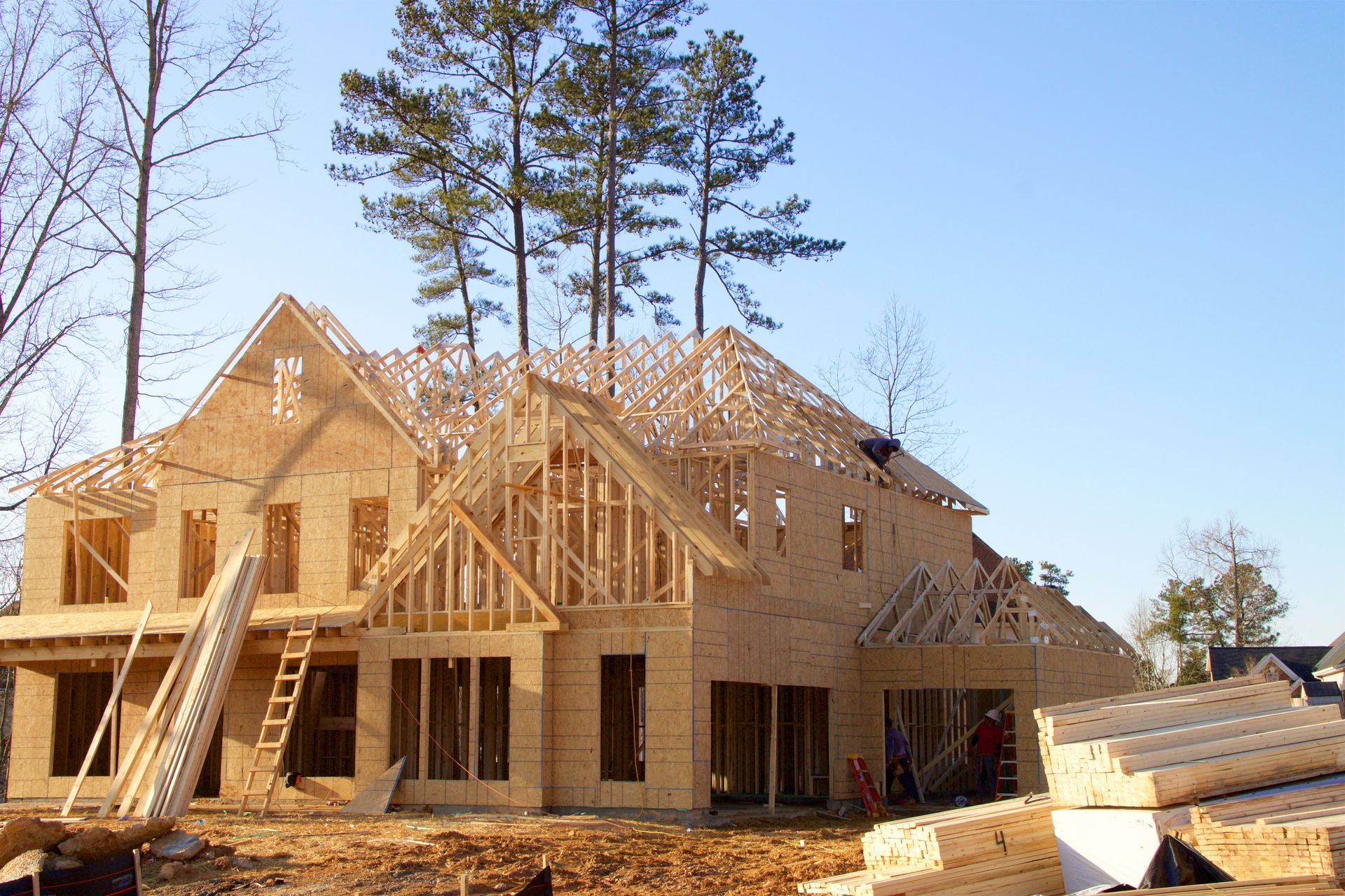 House under construction, wood framing visible, clear blue sky.