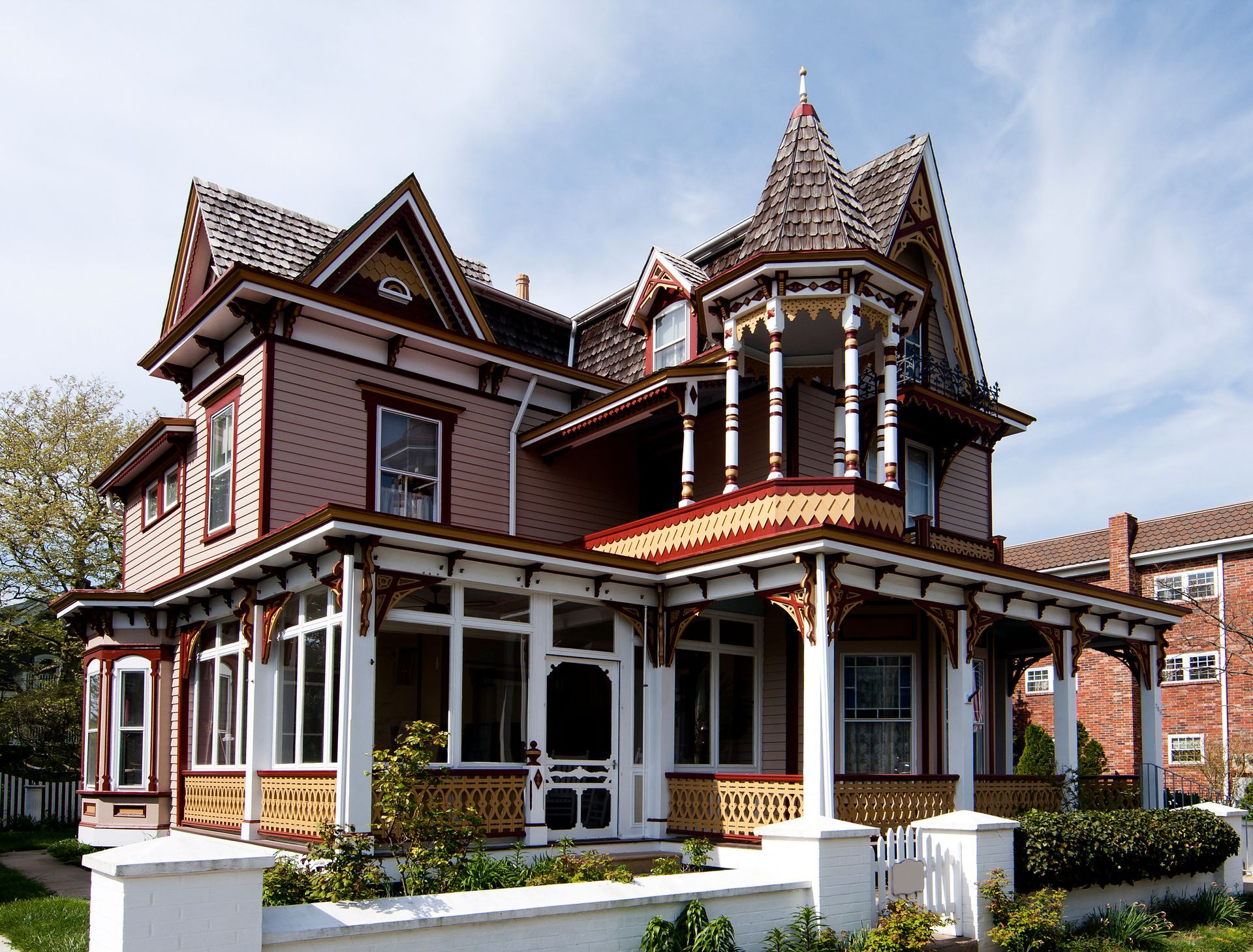 Victorian-style house with pink siding, wrap-around porch, and decorative trim under a blue sky.