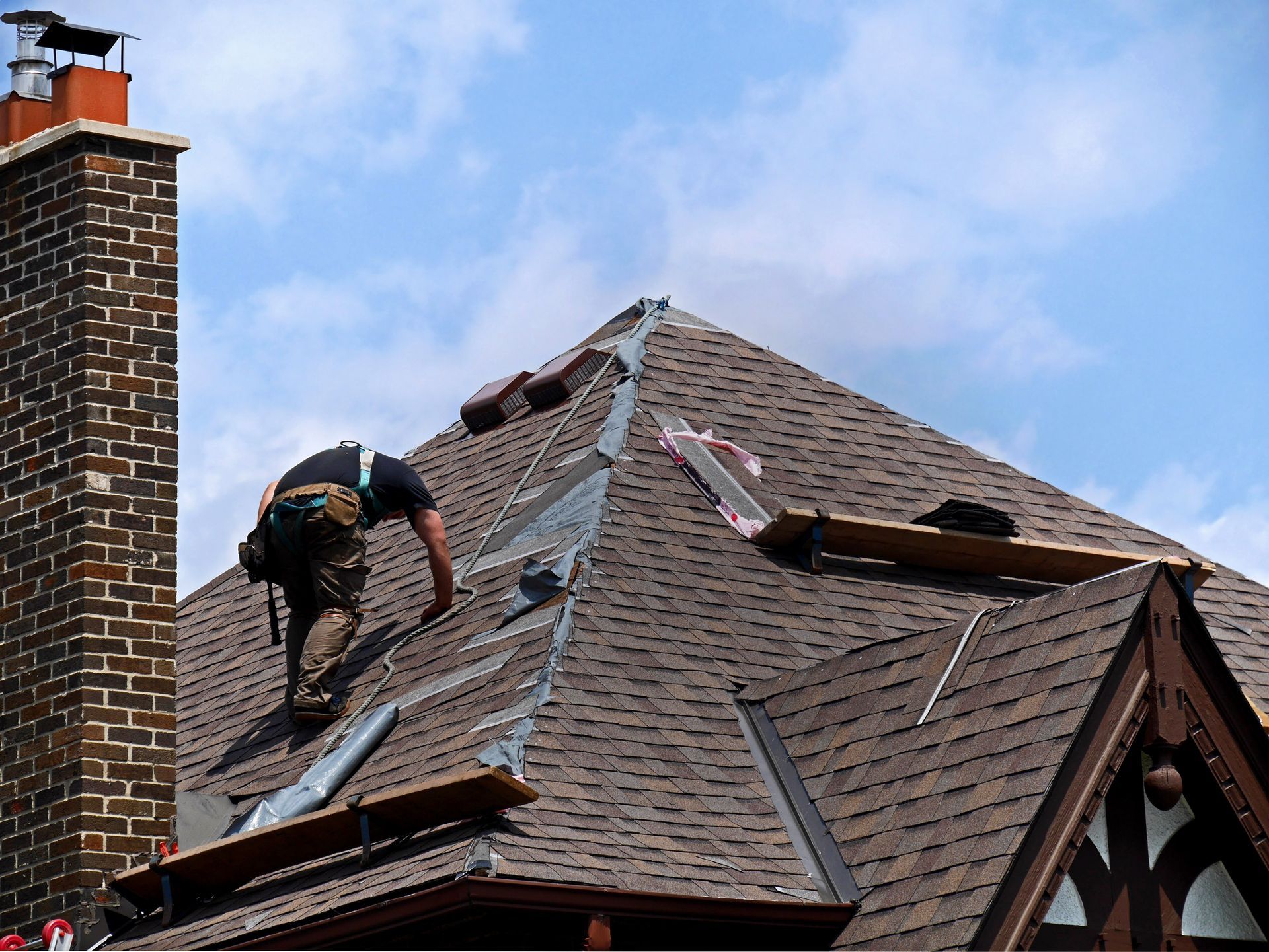 Person replacing roof tiles on a house under a blue sky. Person replacing roof tiles on a house under a blue sky.