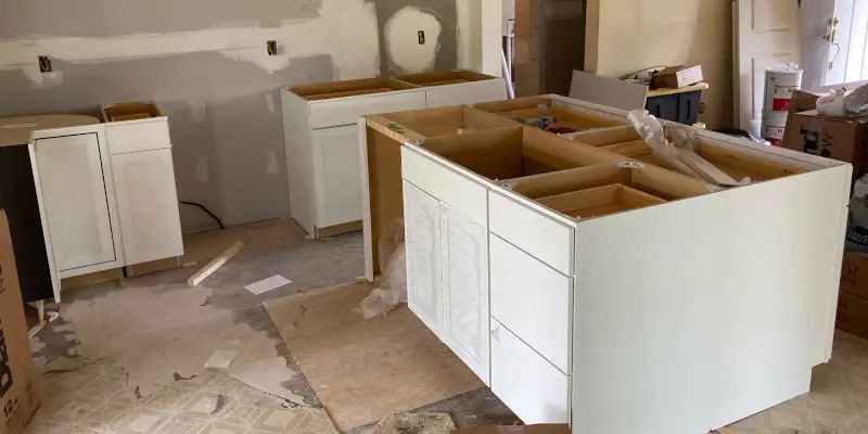 Kitchen under construction, with white cabinetry and an island. Construction materials are scattered