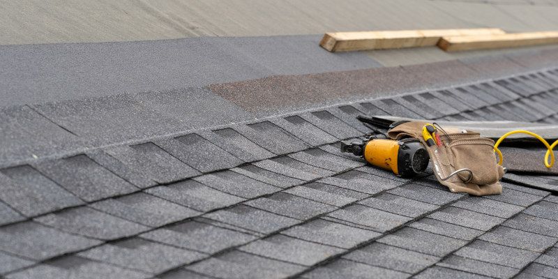 Roofing shingles with a nail gun, belt, and wood on the roof.