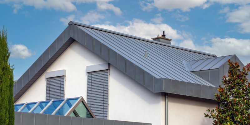 Modern house with gray metal roof against a partly cloudy sky.